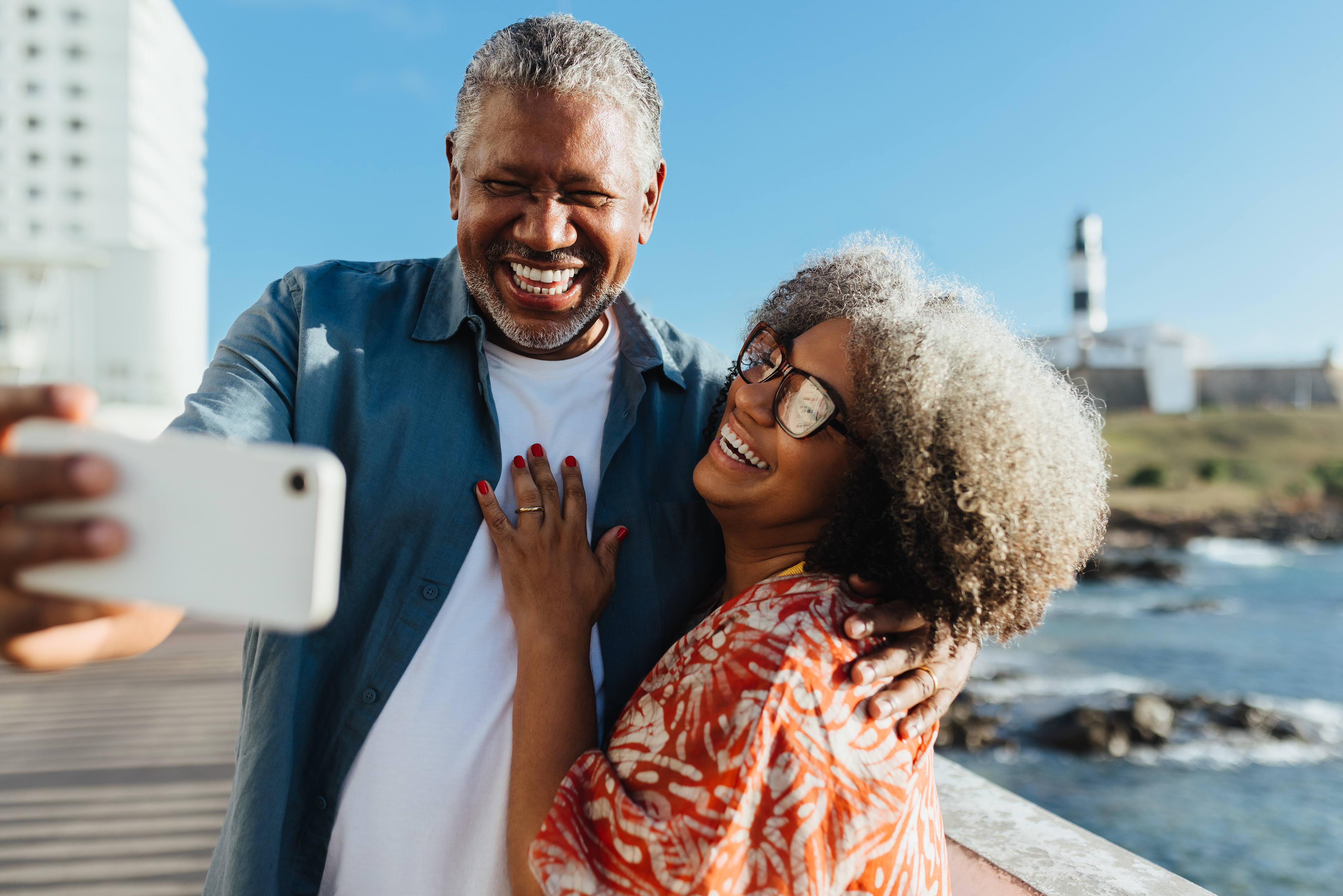 Cheerful senior couple enjoying a sunny day by the sea, taking a selfie to capture their love and happiness in their golden years.
